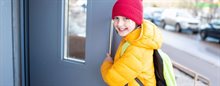 Kind met winterjas en muts dat een deur open houdt.