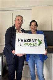 Martijntje van Diessen en Inge Ossenblok met een bord met daarop het logo van Prezent Wonen in hun handen.